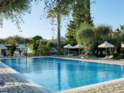 Gran piscina al aire libre rodeada de sombrillas y plantas mediterráneas bajo un cielo azul.