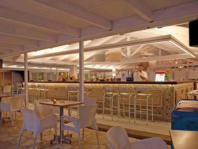 Moderne Bar mit hellen Holzdecken, Stehtischen, weißen Stühlen und Bartresen mit Hockern.