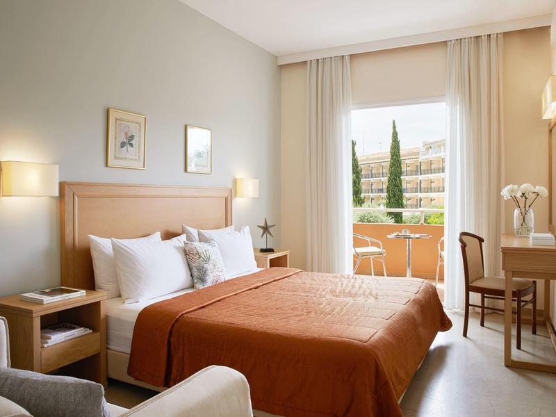 Gemütliches Hotelzimmer mit Doppelbett, Schreibtisch und Balkon mit Blick auf grüne Bäume.