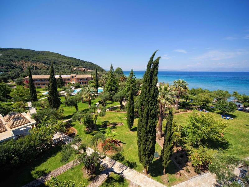 Grüner Garten mit hohen Zypressen neben dem Meer und Hügeln im Hintergrund unter blauem Himmel