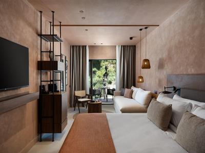 Modernes Schlafzimmer mit großem Bett, Sofa, TV und Zugang zum Balkon mit Pflanzen.