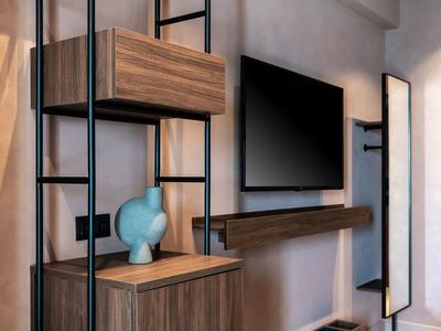 Moderner Wohnraum mit Wandfernseher, Holzregal und blauem Dekokopf auf grauer Wand.