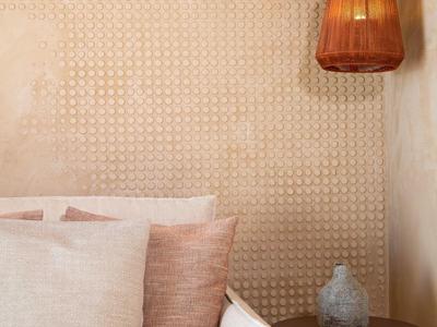 Helles Sofa mit Kissen, Holztisch mit Vase, Wand mit Mustertapete und zwei braune Hängelampen.