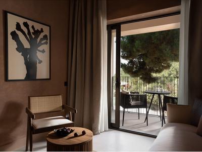 Wohnzimmer mit beige Wänden, Holzstuhl, rundem Holztisch, Sofa und offenem Balkon mit zwei Stühlen.