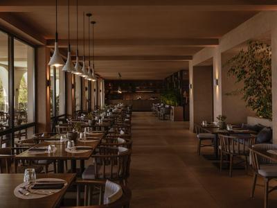Moderner Hotelrestaurant-Speisesaal mit Holztischen und Stühlen, warmem Licht und großen Fenstern.