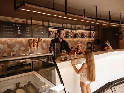 Eine Frau mit Bademantel bestellt an der Theke eines modernen Cafés im Hotel mit warmem Licht.