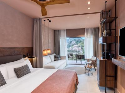 Modern eingerichtetes Hotelzimmer mit Doppelbett, Sitzbereich und Balkon mit Bergblick.