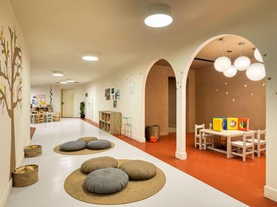 Heller Hotelkinderbereich mit bunten Kissen, Teppichen und Sitzkissen auf orangem Boden.