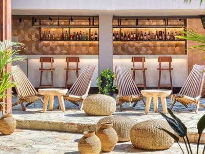 Modernes Outdoor-Hotelbar-Setting mit Holzstühlen, Tischen und Pflanzen auf Steinboden.