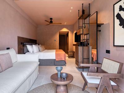 Modernes Hotelzimmer mit Doppelbett, Sofa, Sessel und stilvoller Einrichtung in warmen Tönen.