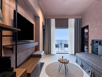 Modern eingerichtetes Hotelzimmer mit gemütlicher Sitzecke und Balkon mit Meerblick.