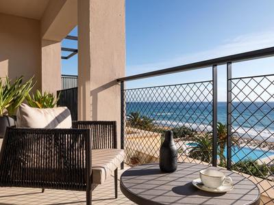 Terrassenbereich mit schwarzem Stuhl, runder Tisch, Pflanzen und Meerblick bei sonnigem Wetter.