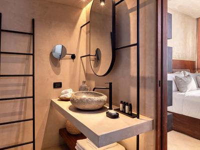 Modernes Badezimmer mit Rundspiegel, goldfarbener Schüssel und schwarzem Wasserhahn neben Schlafzimmer.