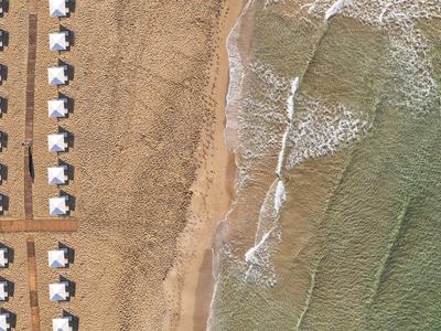 Luftaufnahme eines Strandes mit Reihen von schattigen Liegen und sanften Wellen am Ufer.