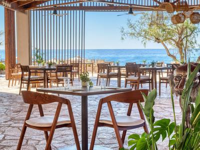 Offenes Restaurant mit Holzstühlen und Blick aufs Meer an einem sonnigen Tag.