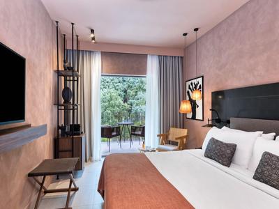 Modern eingerichtetes Hotelzimmer mit Doppelbett und Balkon mit Blick auf Bäume.