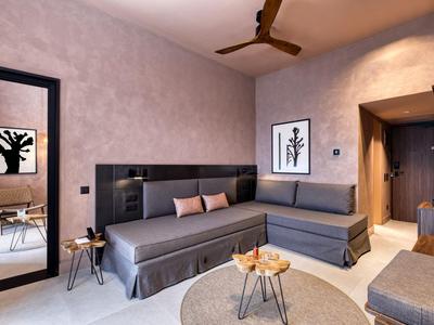 Modern eingerichteter Hotelzimmer mit grauem Sofa, rundem Tisch und Deckenventilator.
