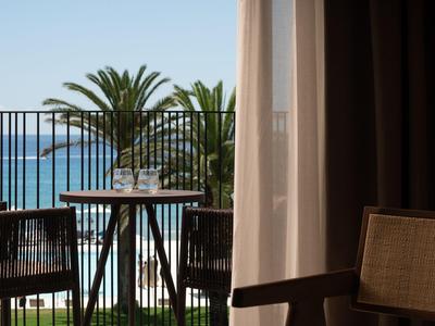 Balkon mit Tisch und Stühlen bietet Aussicht auf Palmen und Meer unter klarem Himmel.