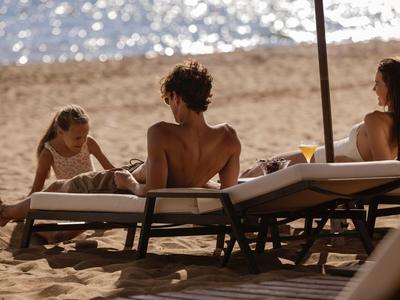 Familie entspannt am Strand auf Liegestühlen mit Blick aufs Wasser.