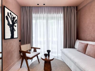 Helles Hotelzimmer mit weißem Sofa, Holzmöbeln und großem Fenster mit Vorhängen.