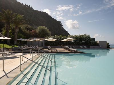 Hotelpool mit Stufen, Sonnenliegen und Blick auf Hügel und Meer bei Tageslicht.