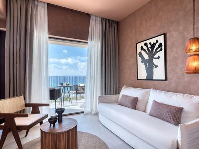 Modern eingerichtetes Wohnzimmer mit Sofa, Sessel, Couchtisch und Meerblick vom Balkon.