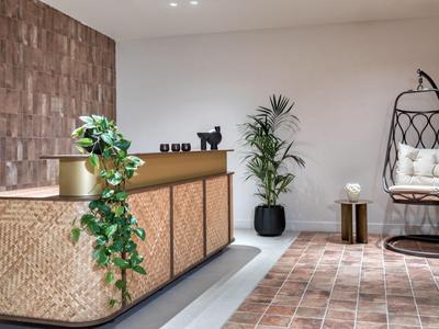 Moderner Hotel-Empfang mit Holztheke, Pflanzen und hängendem Korbsessel auf Fliesenboden.