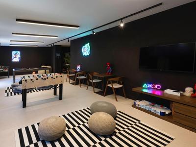 Modernes Hotel-Lounge mit Kickertisch, Schreibtischen, TV und gemütlichen Sitzkissen auf schwarz-weißem Teppich.