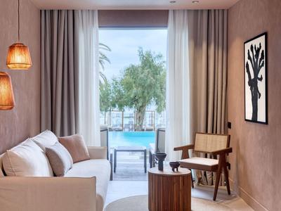 Moderner Hotelraum mit Sofa, Sesseln und Blick auf einen Pool und Palmen.
