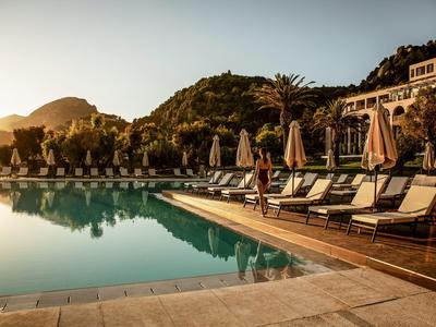 Ein ruhiger Poolbereich mit Liegestühlen und Sonnenschirmen bei Sonnenuntergang neben einem Hotel.
