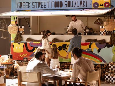 Eine griechische Straßenimbissbude mit Menschen, die Souvlaki und andere Speisen genießen.