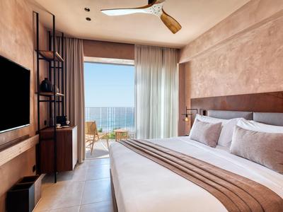 Modernes Hotelzimmer mit Meerblick, Doppelbett und Balkon mit Stühlen.