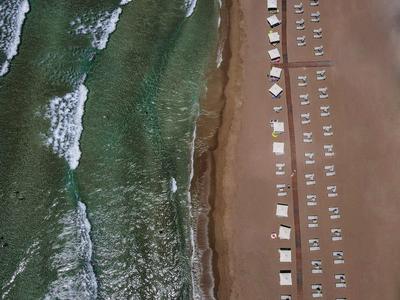 Strand mit sanften Wellen, Reihen von weißen Liegestühlen und Sonnenschirmen auf braunem Sand.