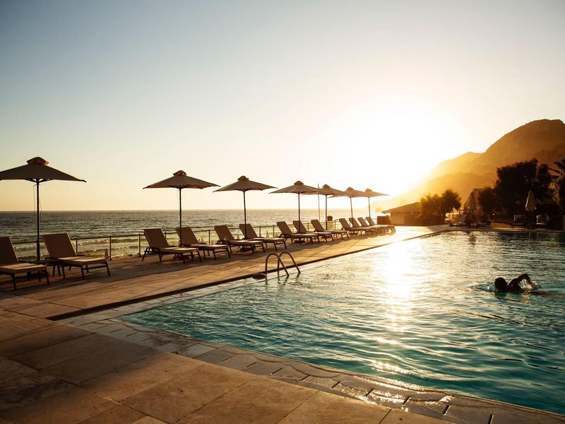 Ein Außenpool mit Sonnenliegen und Schirmen bei Sonnenuntergang am Meer.