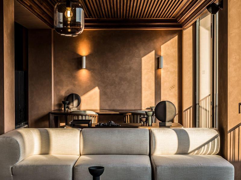 Modernes Wohnzimmer mit cremefarbenem Sofa, Holzwänden und großen Fenstern bei warmem Licht.