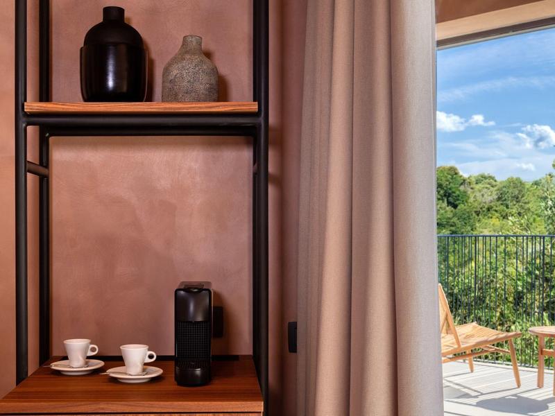 Wohnzimmer mit braunem Regal, Kaffeetassen, Kaffeemaschine und Blick auf Terrasse mit grüner Natur.