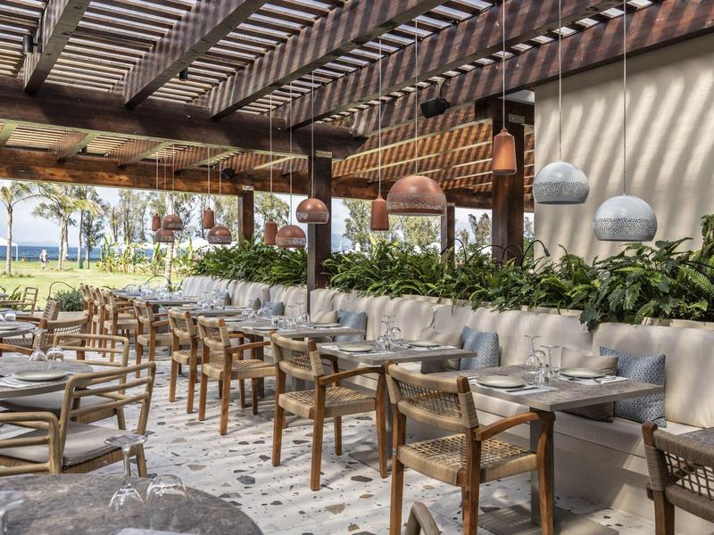 Offenes Restaurant mit Holzpergola, Holztischen, Stühlen und grünen Pflanzen als Dekoration.