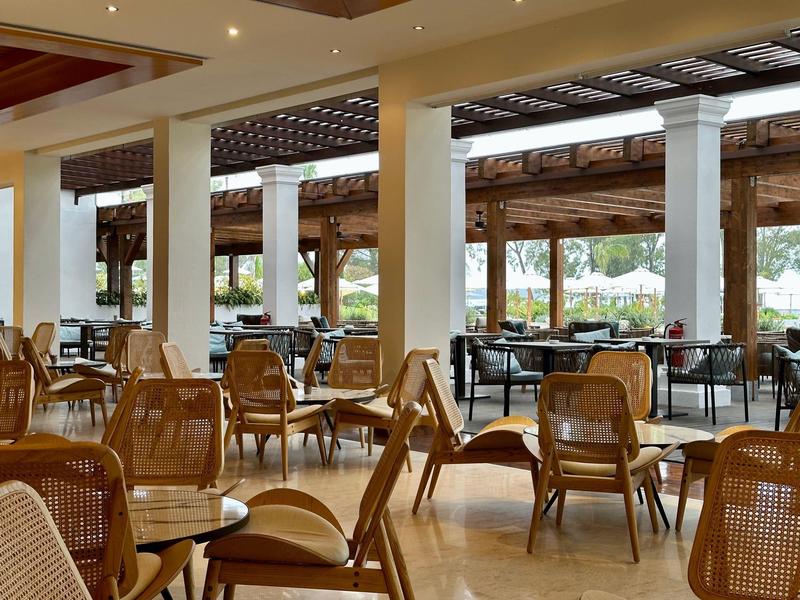 Hell eingerichteter Essbereich mit Holzstühlen und Tischen, große Fenster mit Außenblick.