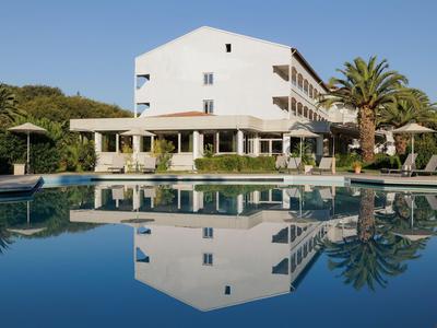 Ein Hotelgebäude spiegelt sich in einem klaren Swimmingpool mit Palmen und Sonnenschirmen.