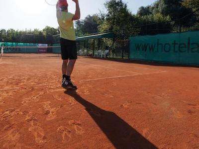 Person spielt Tennis auf einem Sandplatz bei Sonnenlicht mit langem Schatten.