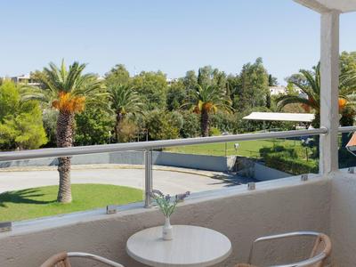 Balkon mit zwei Stühlen und kleinem runden Tisch, Blick auf grüne Palmen und blauen Himmel.