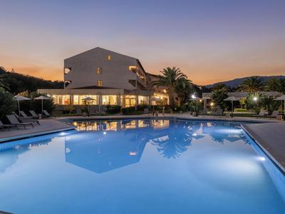Beleuchteter Hotelpool bei Sonnenuntergang mit Liegestühlen und Bergen im Hintergrund.
