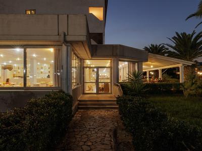 Abendaufnahme eines beleuchteten modernen Gebäudes mit angrenzendem Außenbereich und Pflanzen.