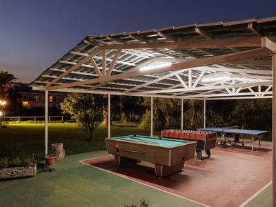 Überdachter Außenbereich mit Billardtisch und Sitzgelegenheiten in einer Gartenanlage bei Dämmerung.