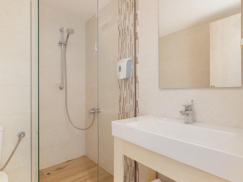 Modernes Badezimmer mit Dusche, weißem Waschbecken, großem Spiegel und hellen Fliesen.