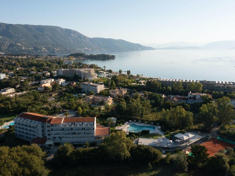 Blick auf Küstenstadt mit Bergen, Gebäuden, Swimmingpools und ruhigem Meer im Hintergrund.
