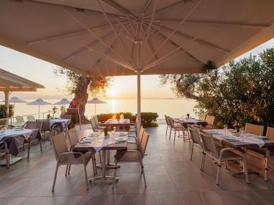 Sunny restaurant terrace with tables and chairs by the sea at sunset.
