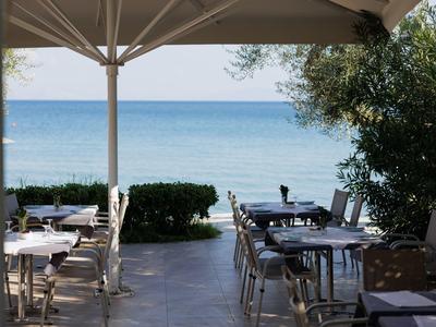 Blick von einer überdachten Terrasse mit Tischen und Stühlen auf das blaue Meer und Himmel.