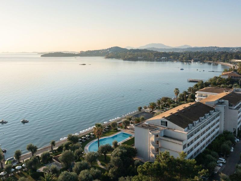 Blick auf Küstenlinie mit ruhigem Meer, Hotels, Swimmingpools und Palmen bei klarem Himmel.