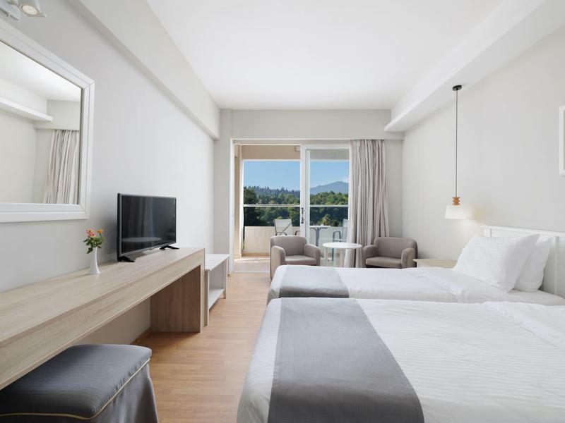 Helles Hotelzimmer mit Doppelbett, Flachbildschirm, großem Spiegel und Balkon mit Meerblick.